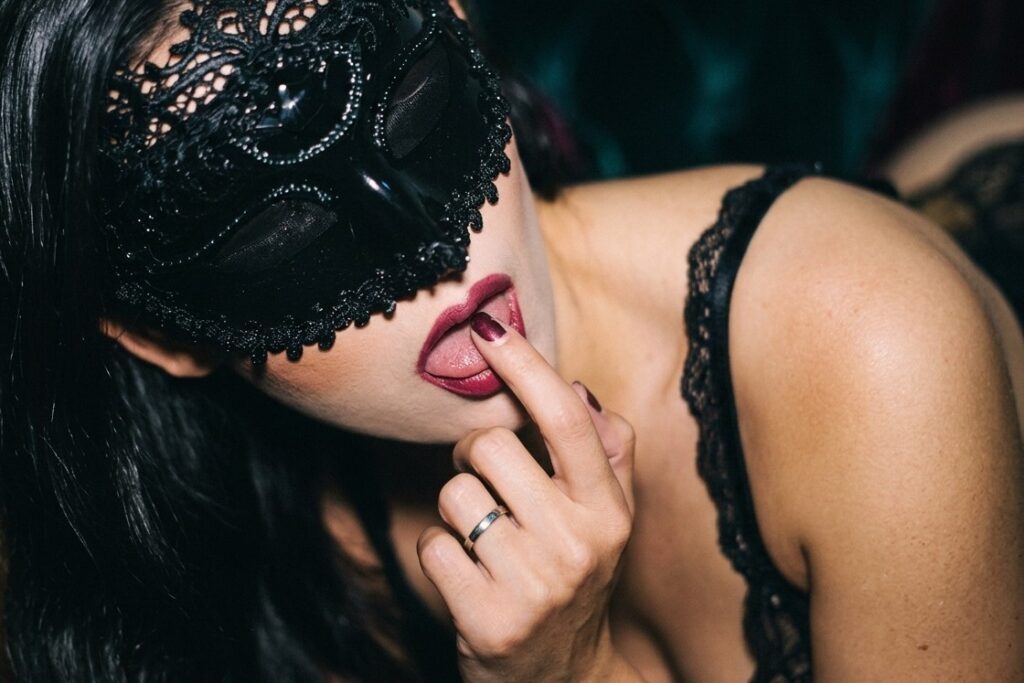 黒いレースのマスクで目元を隠し唇に指を触れる女性
